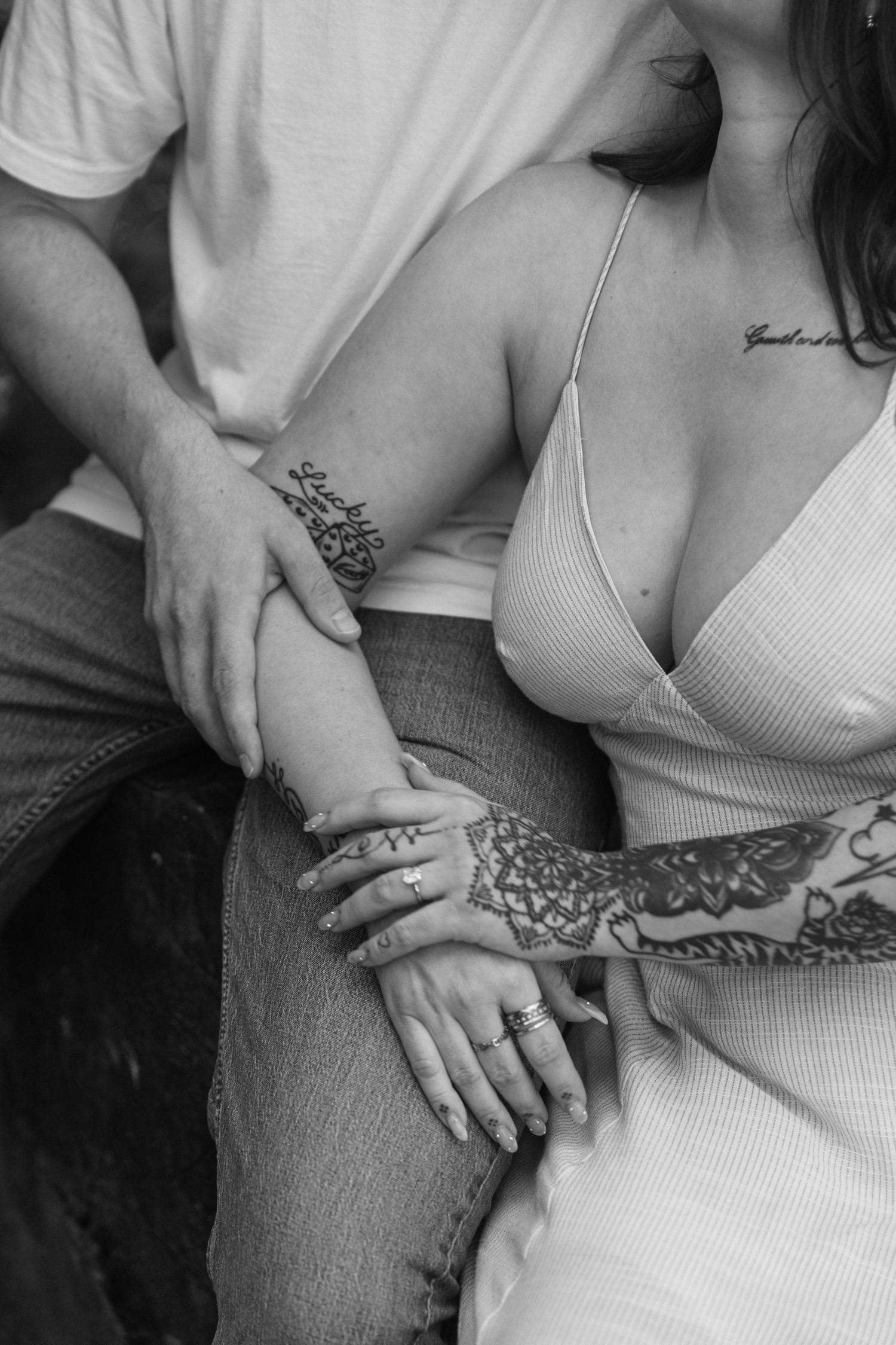 A close-up black and white photo focusing on intertwined hands and intricate tattoo details.