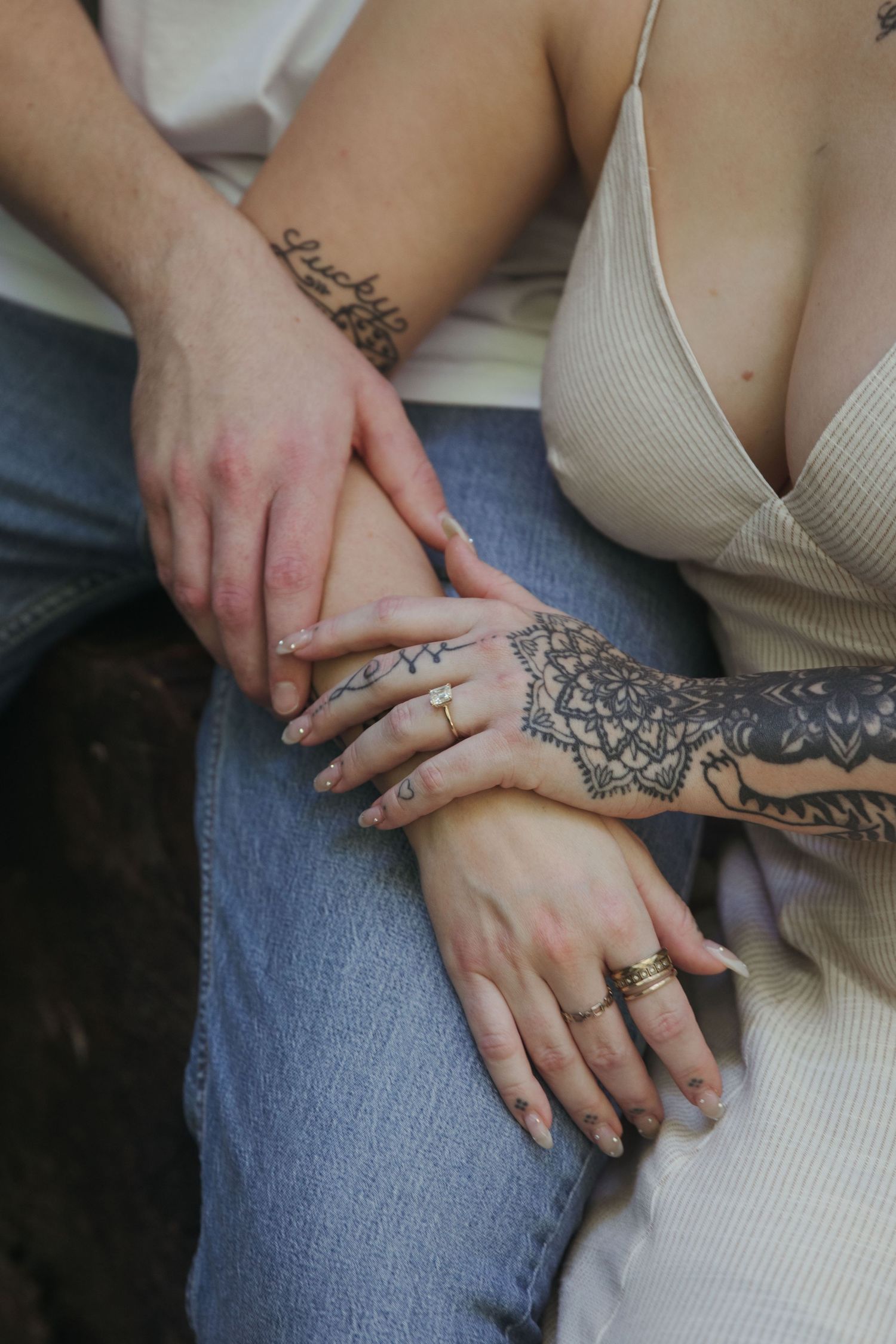 A detailed shot of hands touching, showcasing intricate tattoo work and engagement rings.