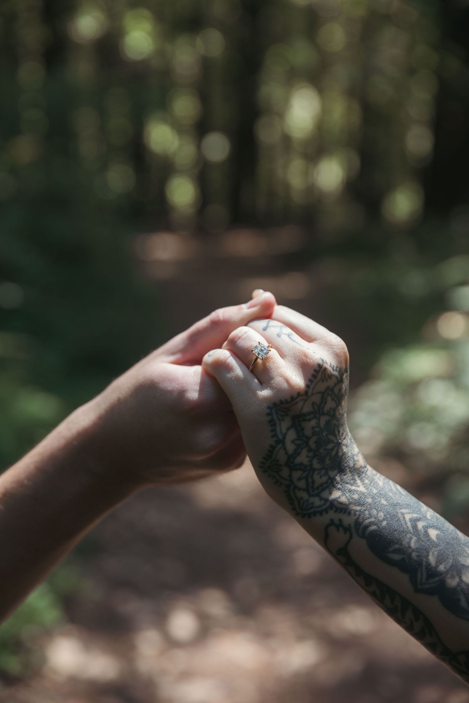 Two hands clasp together in the forest, one with intricate tattoo artwork.