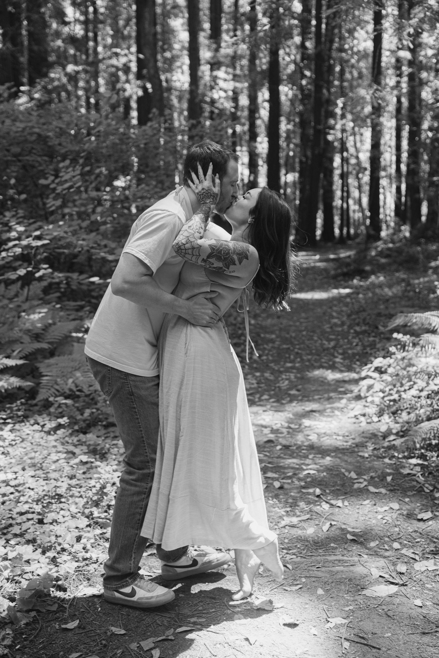 A romantic embrace between a couple on a wooded path in black and white.