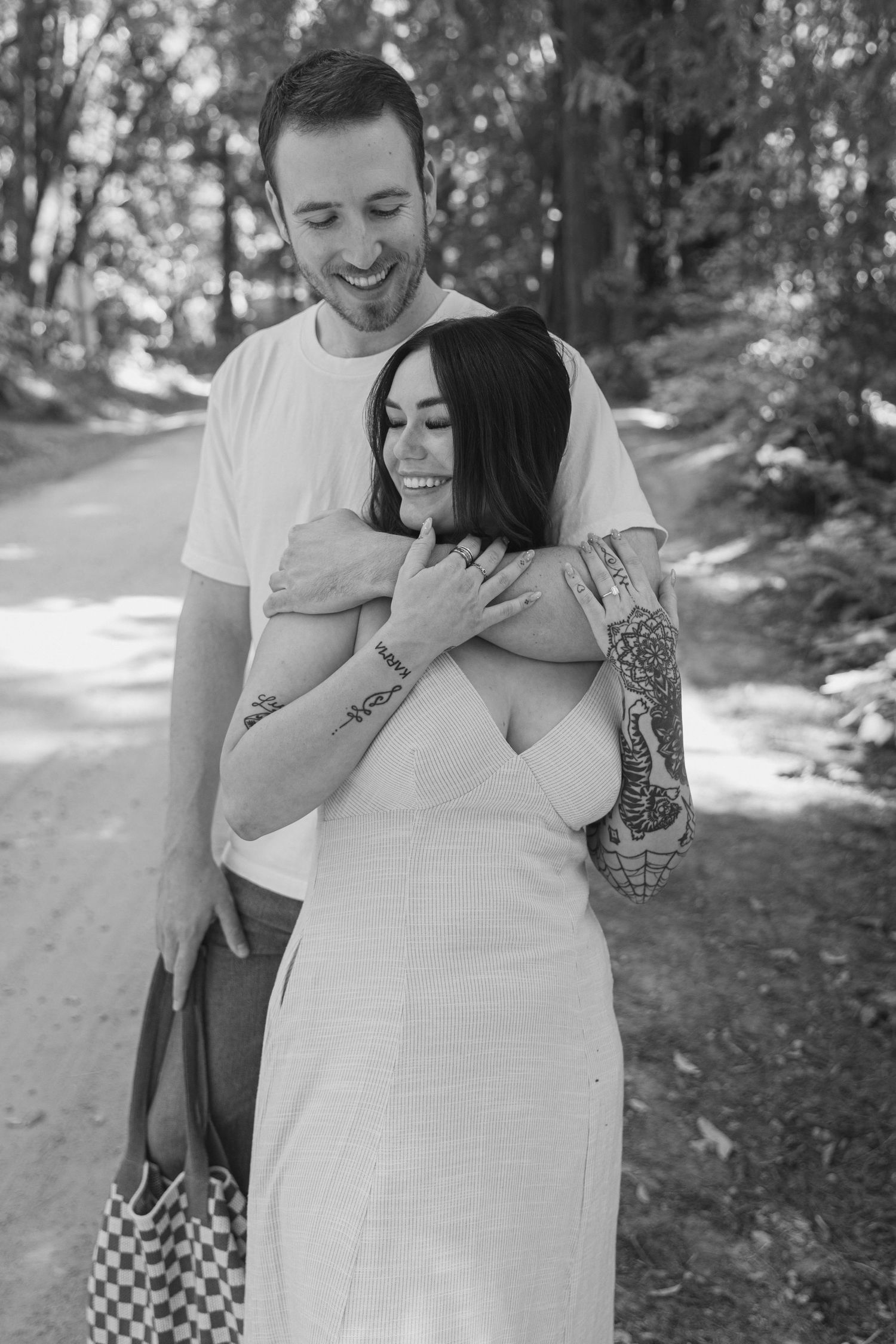 A romantic embrace between a couple on a wooded path, with the woman wearing a white dress and man in casual attire.