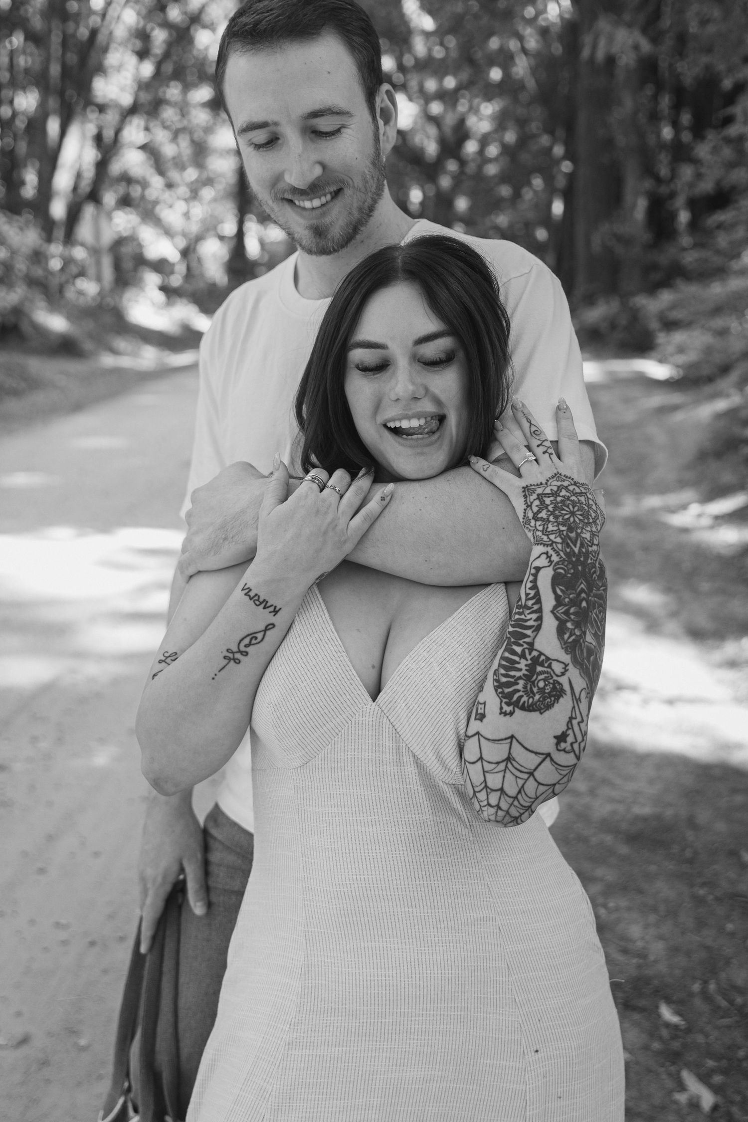 Joyful couple sharing a candid moment outdoors, with visible tattoos and natural forest backdrop.