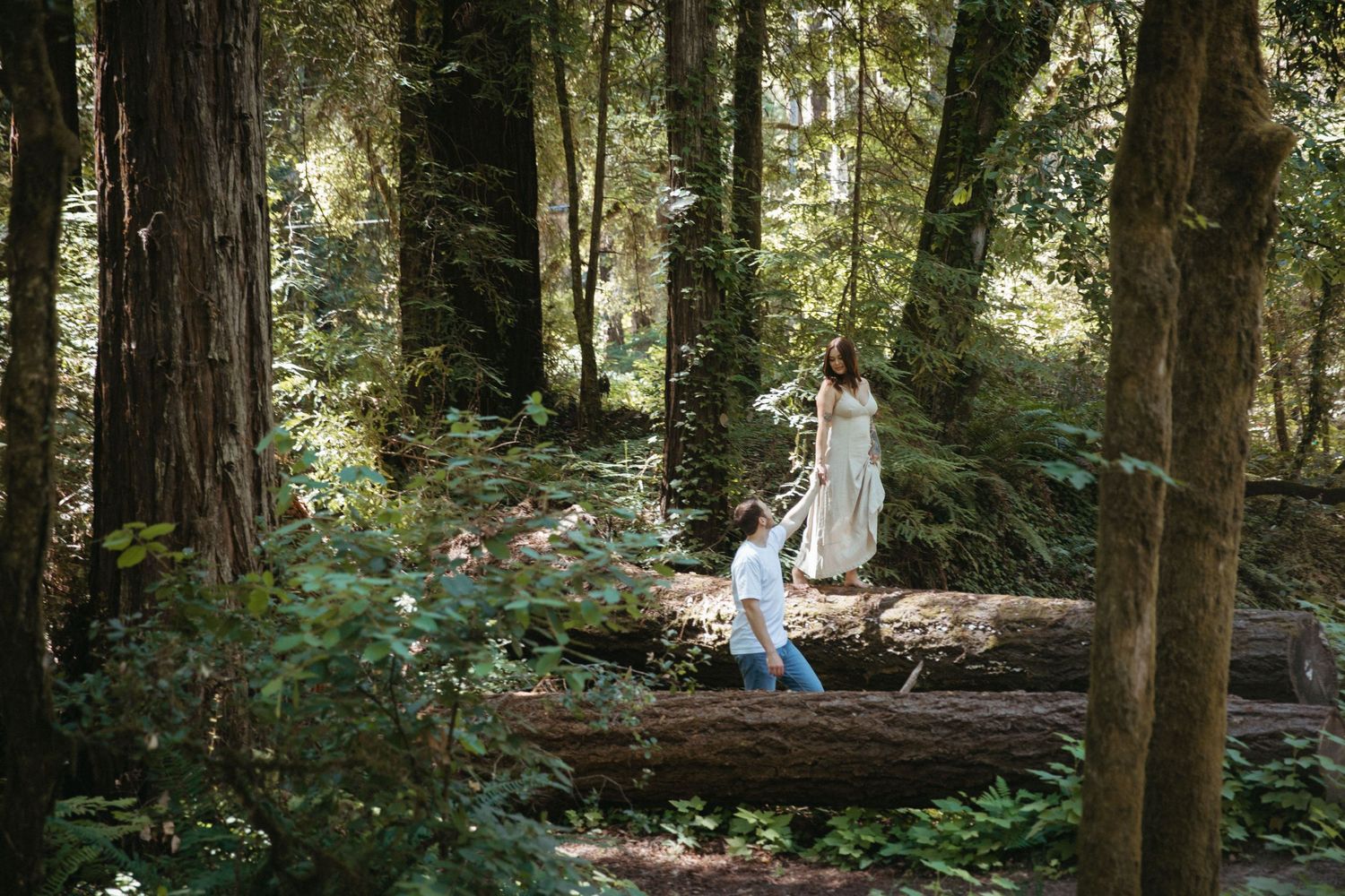 Couple sitting on fallen log in sunlit forest clearing.