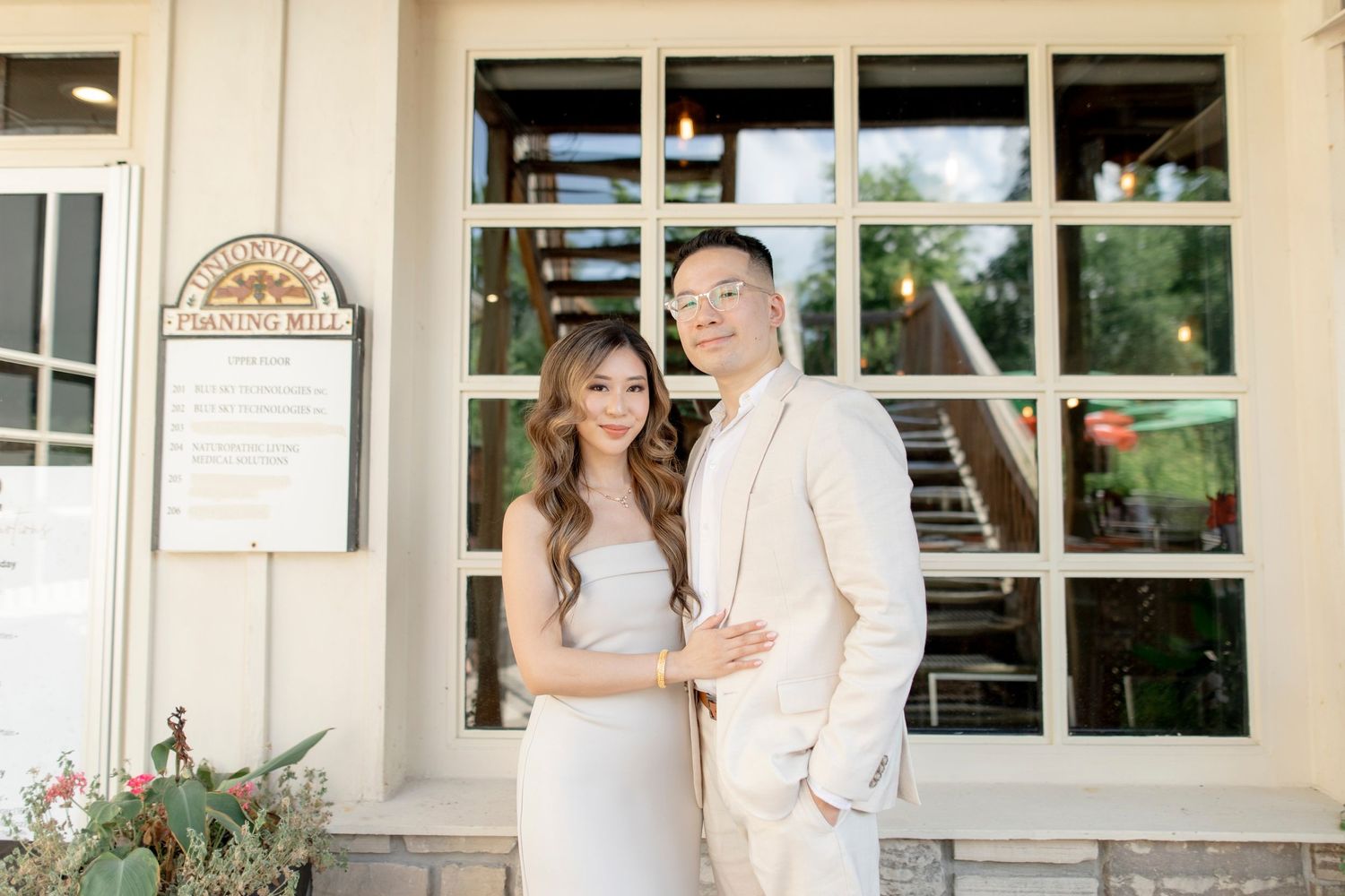 Elegant couple in matching cream outfits pose against a building's exterior.