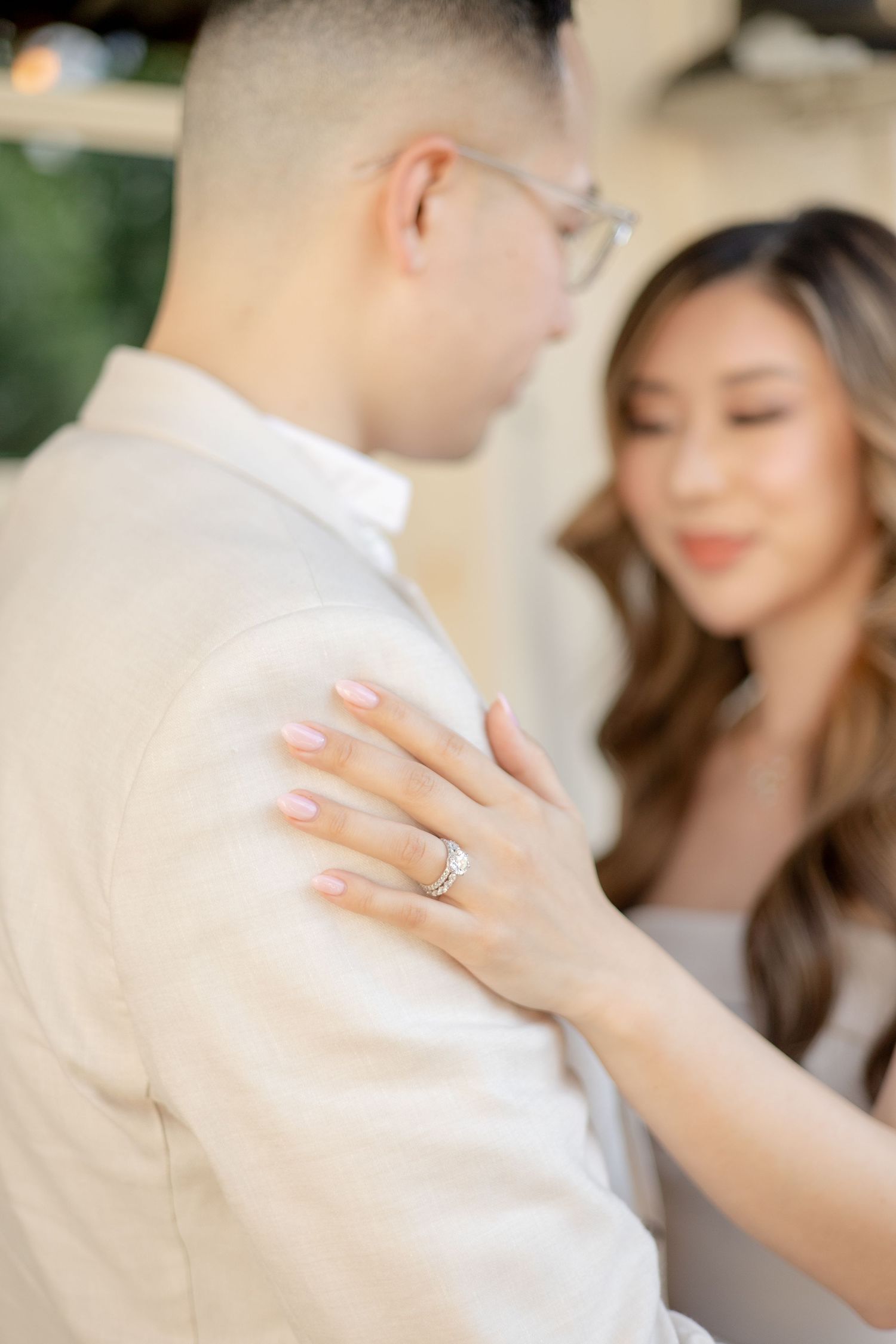 A tender moment between a couple showing off an engagement ring against neutral toned clothing.