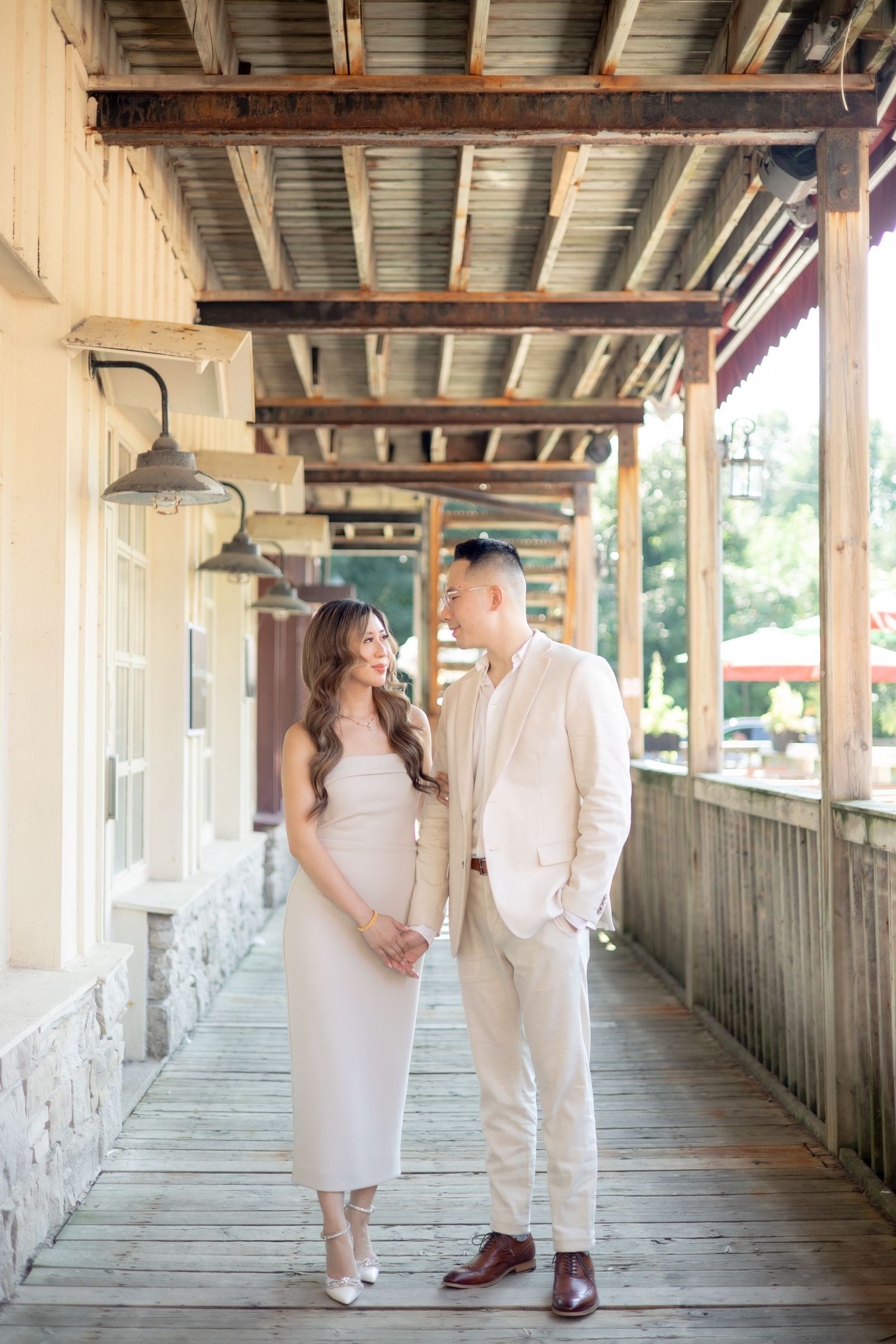 A stylish couple stands together on a rustic wooden porch with industrial pendant lights overhead.