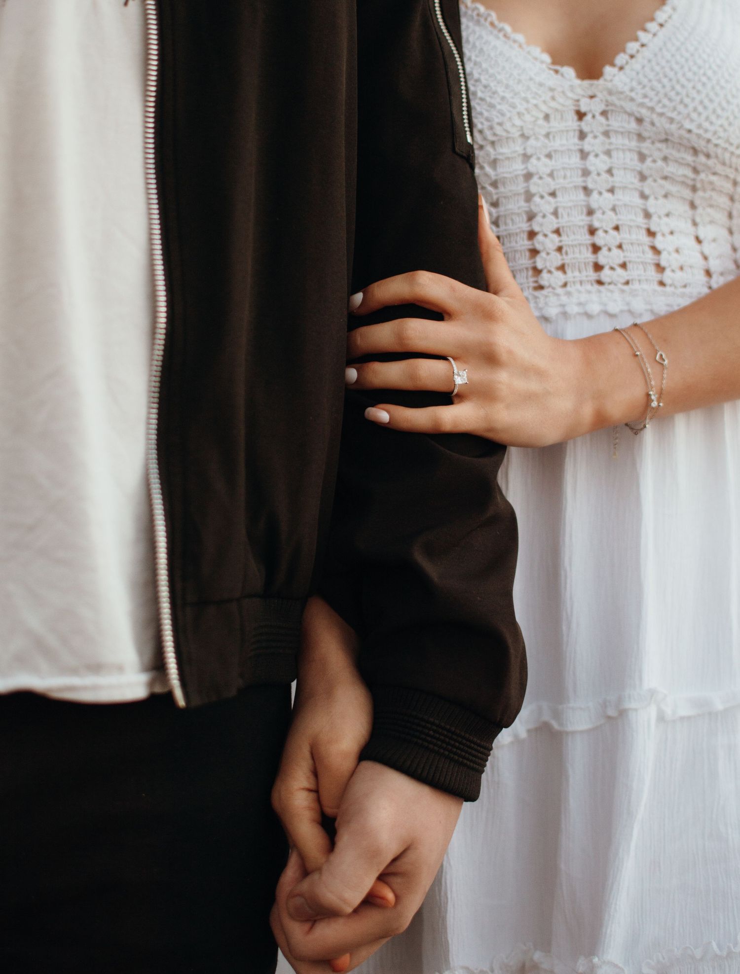 Close-up of hands showing engagement ring detail against black and white formal attire.