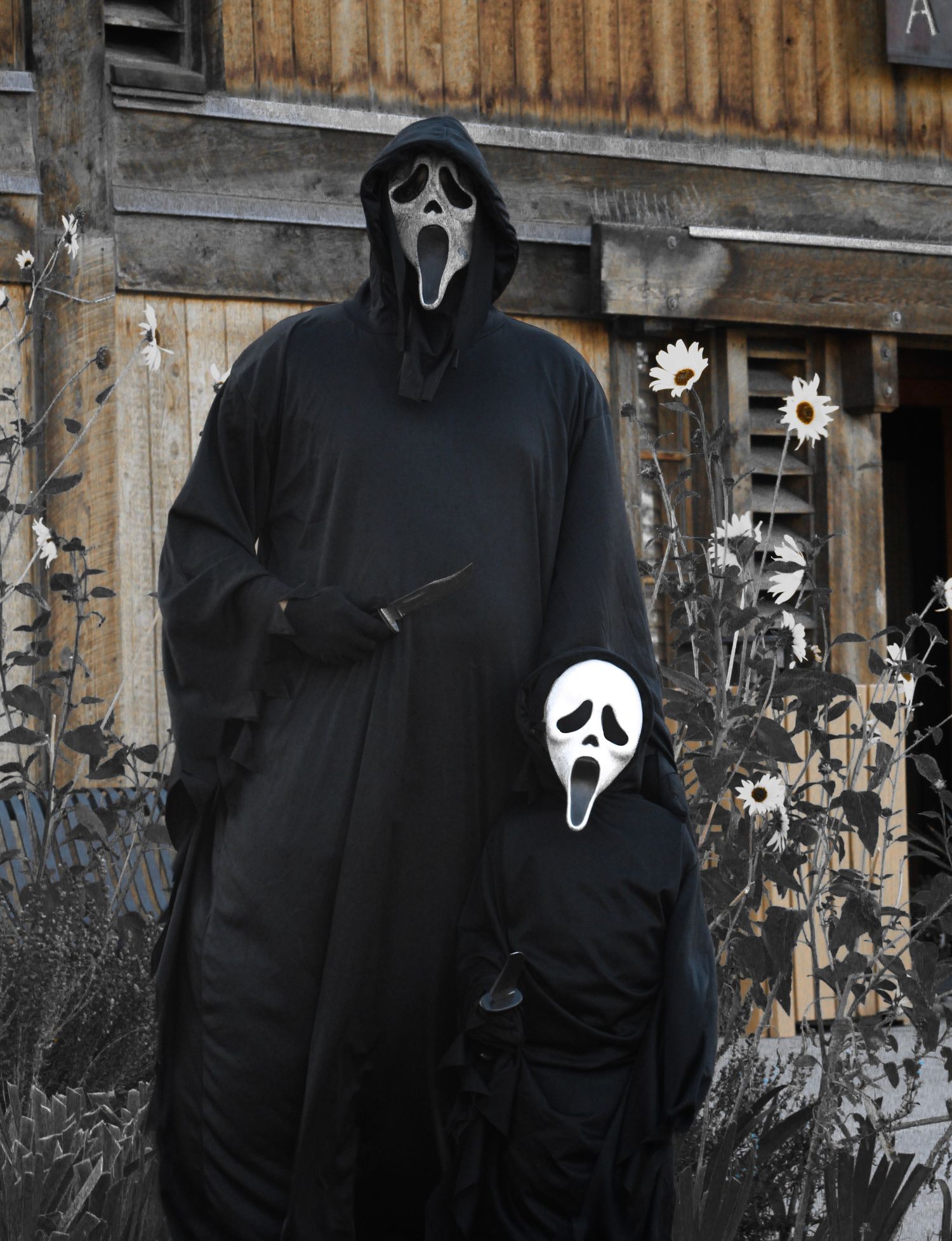 Two people in Ghostface costumes pose near a rustic wooden building with flowers.