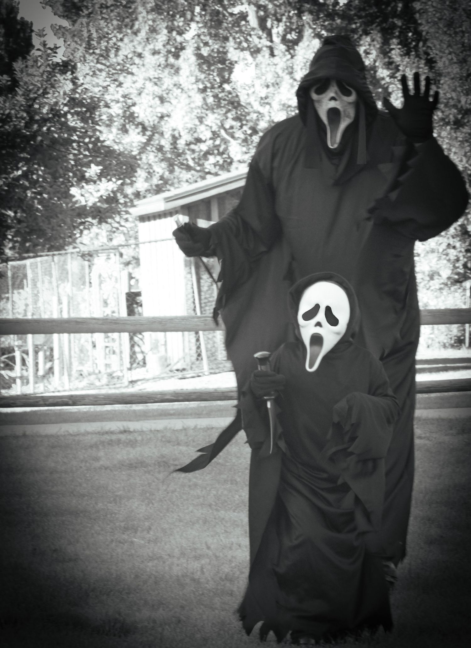 Two Ghostface costume wearers pose dramatically outdoors in black and white.