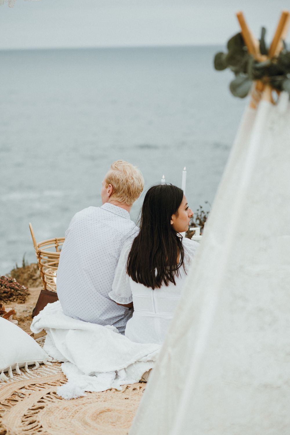 A couple enjoys a romantic picnic at Sunset Cliffs as the sun sets, capturing the moment of their engagement proposal.