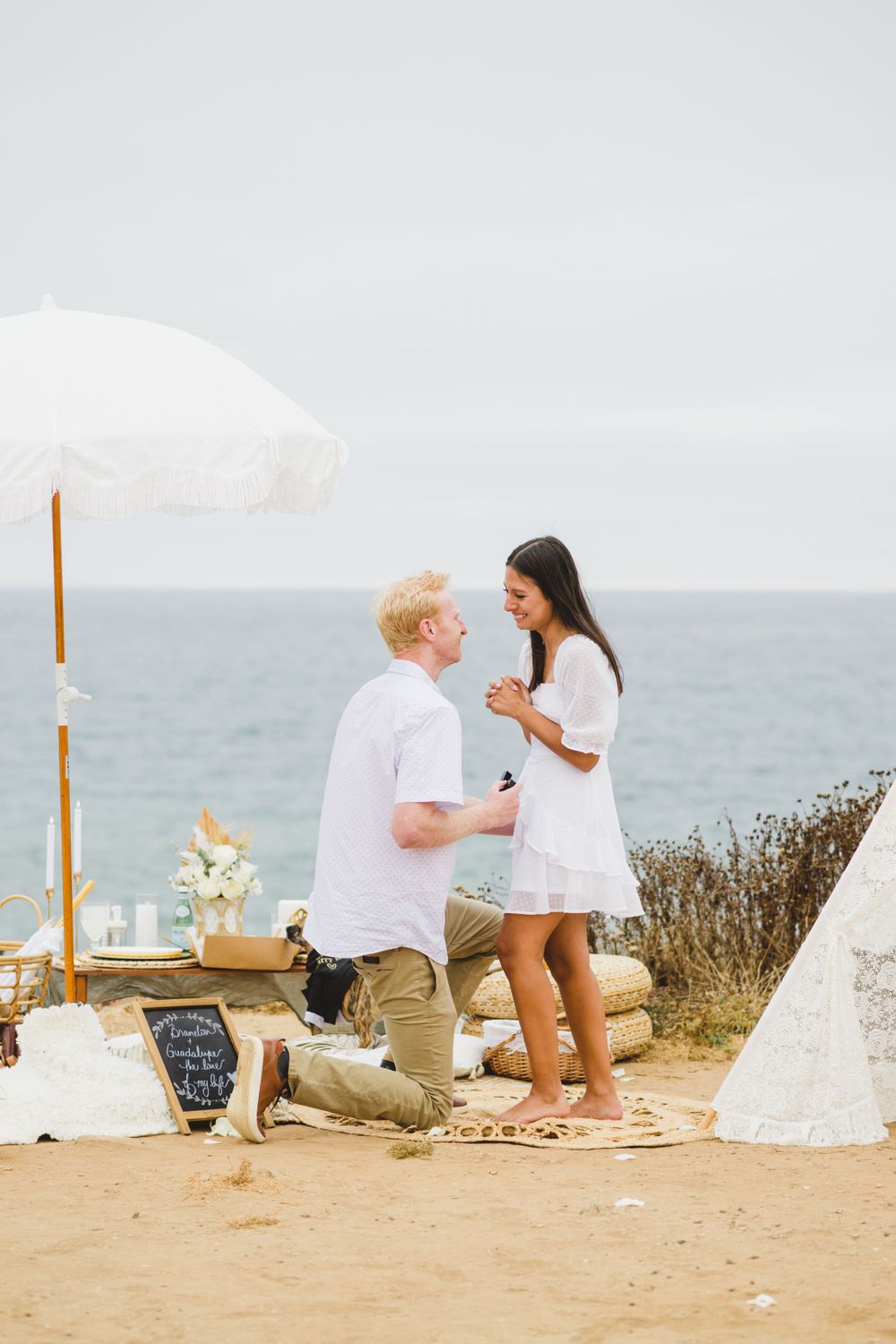 A couple enjoys a romantic picnic at Sunset Cliffs as the sun sets, capturing the moment of their engagement proposal.