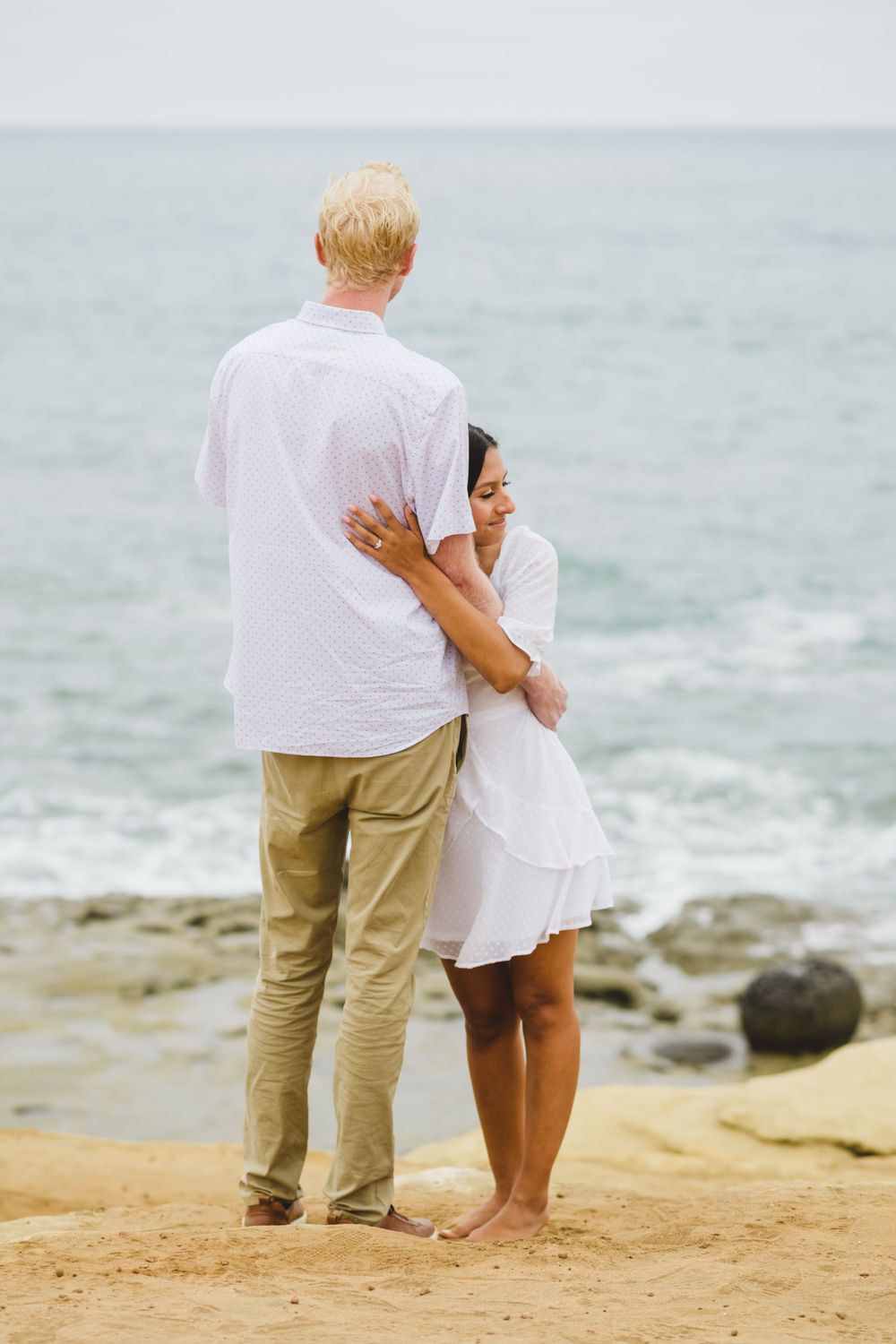 A couple enjoys a romantic picnic at Sunset Cliffs as the sun sets, capturing the moment of their engagement proposal.