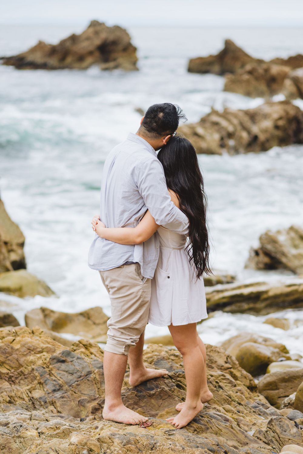 A couple poses for engagement photos at Corona del Mar, capturing the romance and natural beauty of the beach.