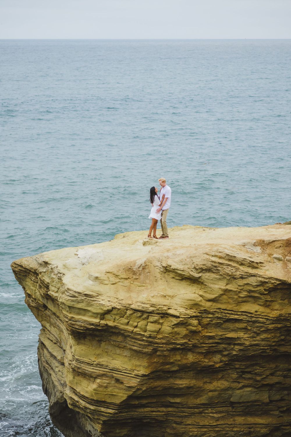 A couple takes their engagement photos at Sunset Cliffs as they embrace during sunset.