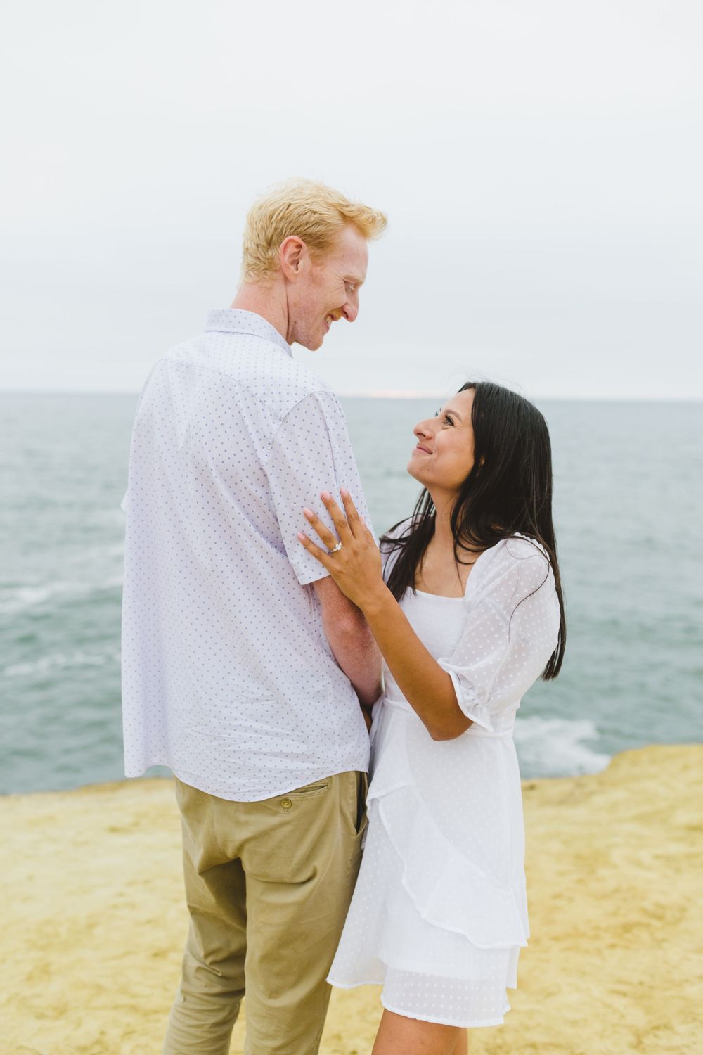 A couple takes their engagement photos at Sunset Cliffs as they embrace during sunset.