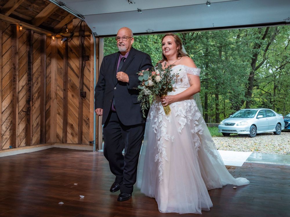 Wedding ceremony entrance at wooden venue with car visible in background.