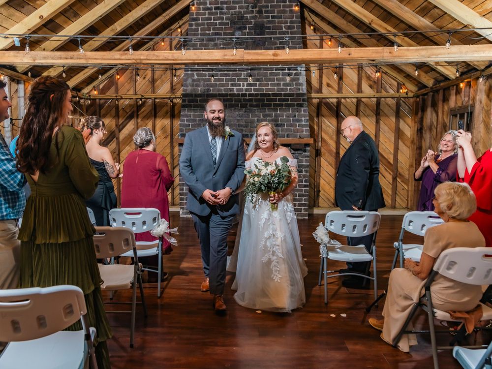 A rustic barn wedding ceremony with exposed wooden beams and brick walls.