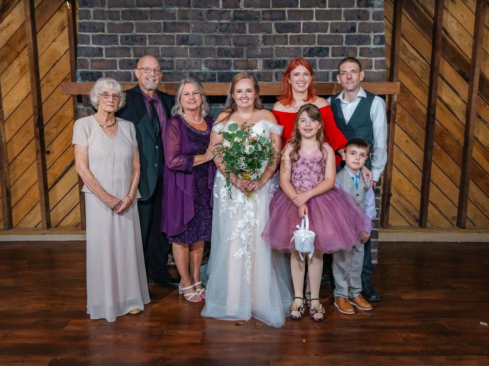 Wedding party poses together in formal attire against wooden doors and brick wall background.