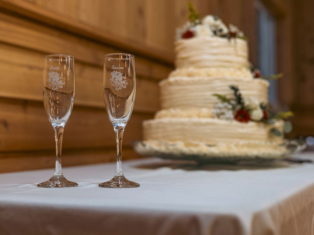 Two champagne flutes in front of an elegant wedding cake on a white tablecloth.