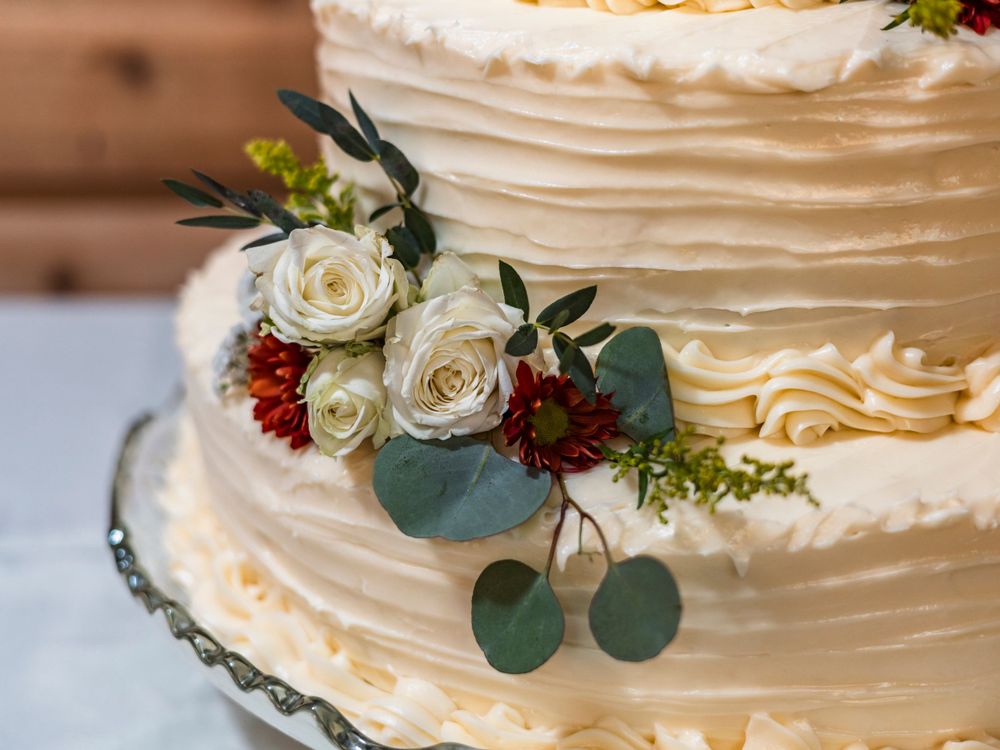 An elegant white wedding cake decorated with roses and eucalyptus leaves.