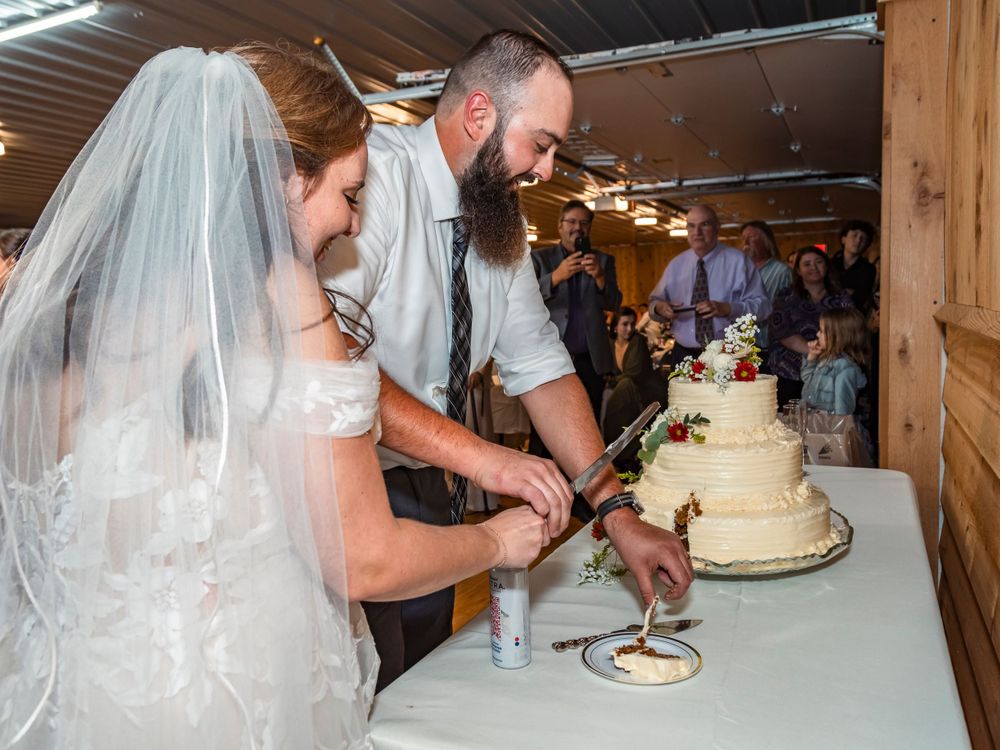 A wedding couple cutting their traditional white tiered cake together.