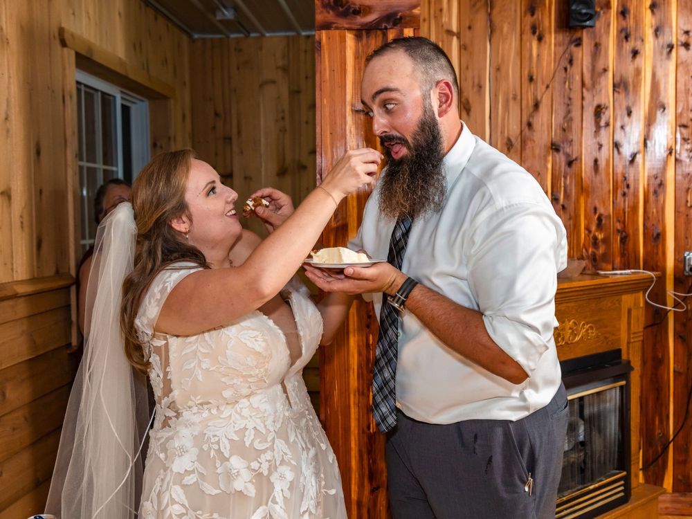 A couple playfully sharing their wedding cake at a rustic venue.