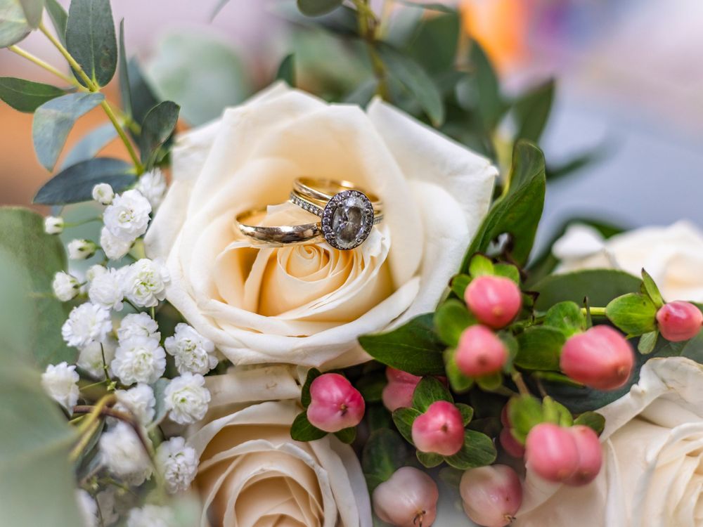 Wedding rings nestled in white roses with pink berries and baby's breath floral arrangement.
