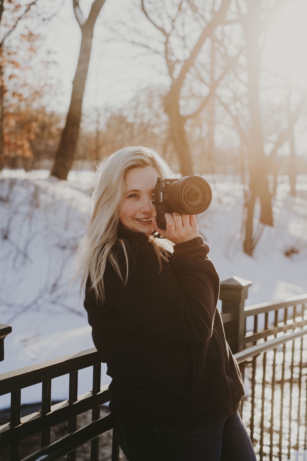 Photographer in black coat takes pictures in snowy winter landscape.
