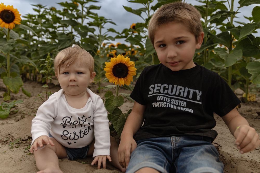 Children sit together among tall blooming sunflowers in a garden setting during summer.