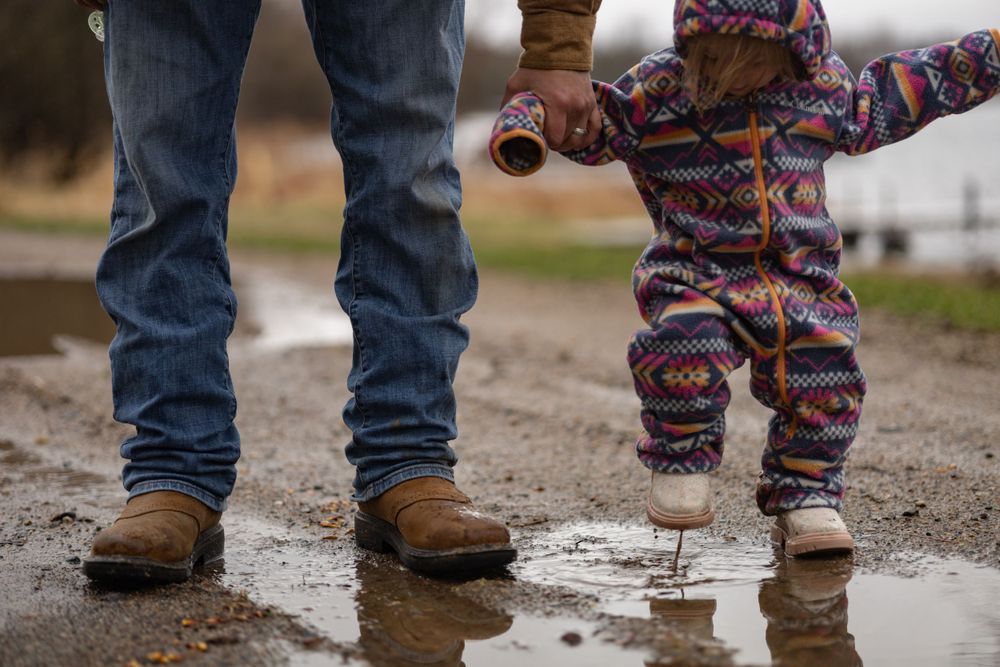 Two pairs of boots splashing in a muddy puddle on a rainy day.