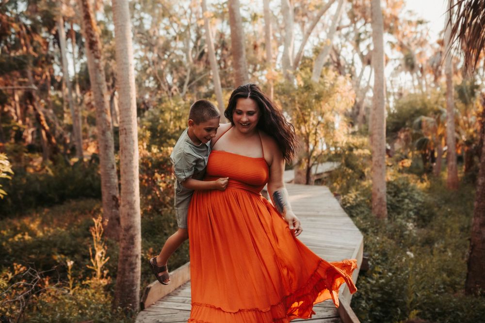 Two people embrace on a wooden boardwalk surrounded by tall trees during golden hour.
