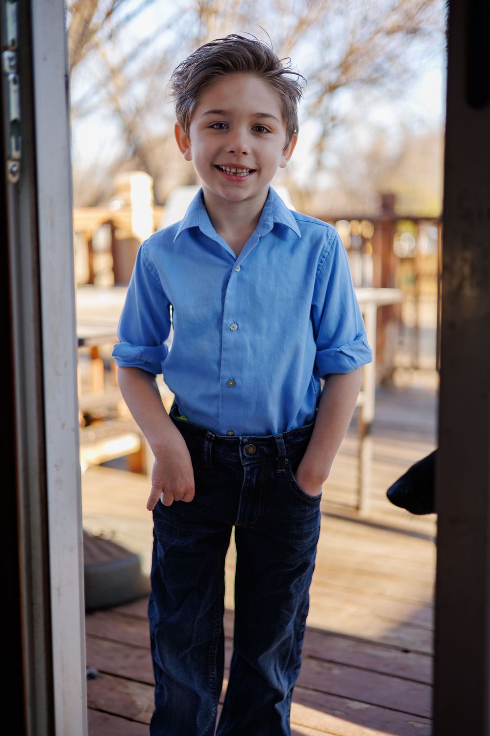 Young person in blue polo shirt and jeans standing on wooden deck during golden hour.