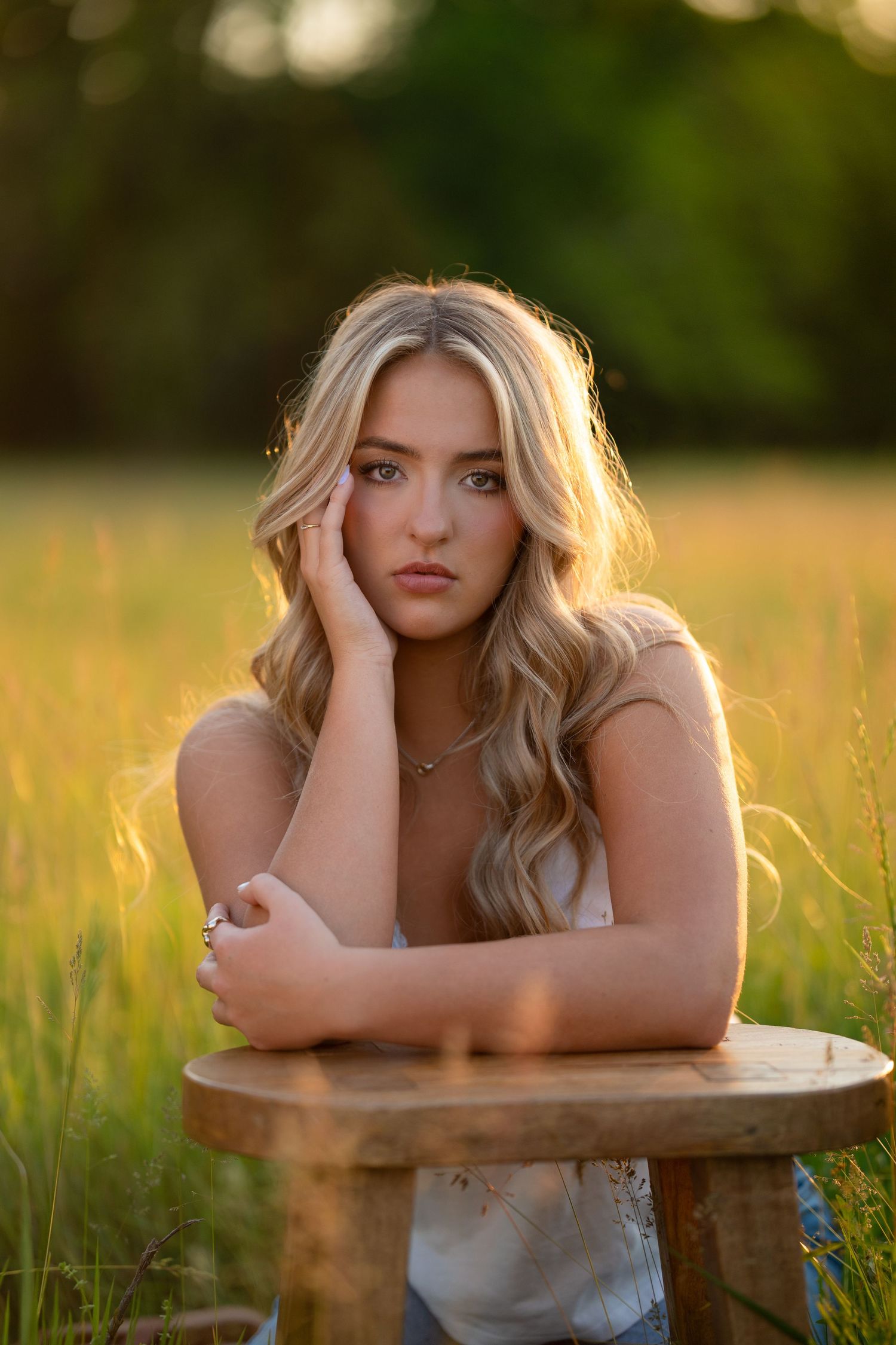 Middle Tennessee Senior Portrait of a young woman in a white sweater and pink scarf smiling at sunset with backlit golden light.