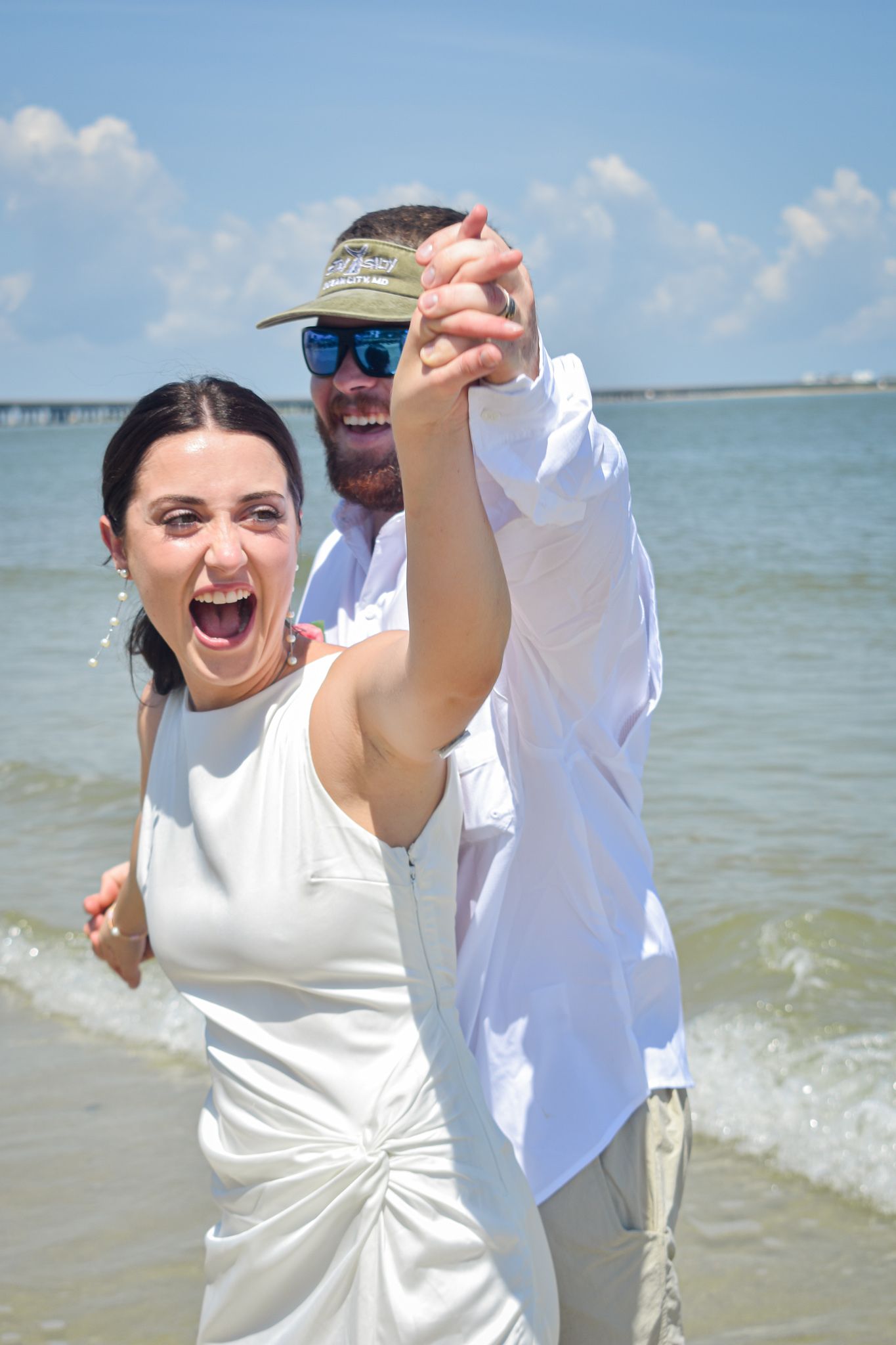 A joyful couple celebrates with raised hands on a sunny beach.