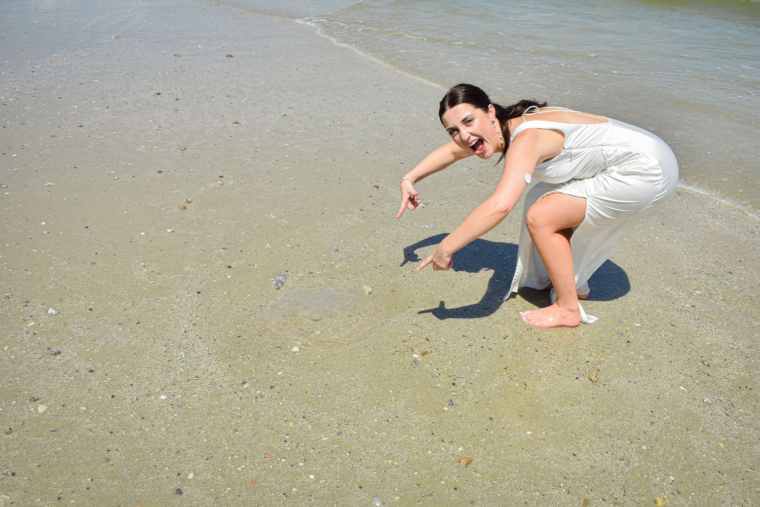 Person in white dress searching for shells on a sandy beach.