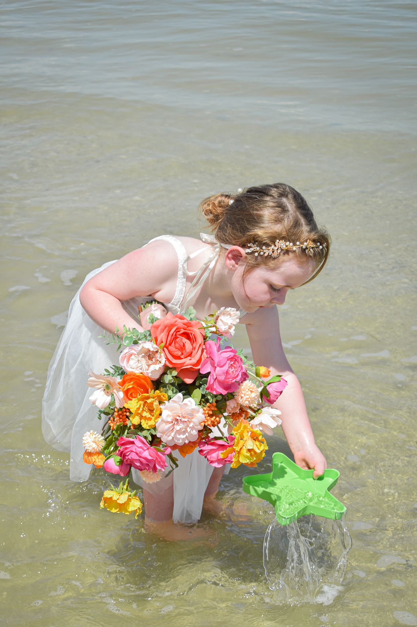 Young attendant in white dress with flower crown collecting water at beach.