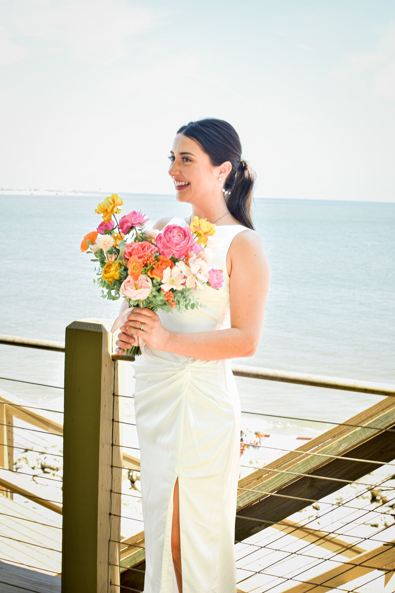 Wedding moment captured on oceanfront deck with colorful floral bouquet.