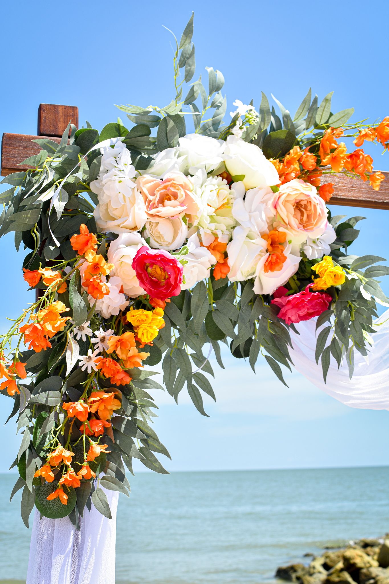 Floral arch with orange and pink blooms against ocean backdrop for beach wedding ceremony.