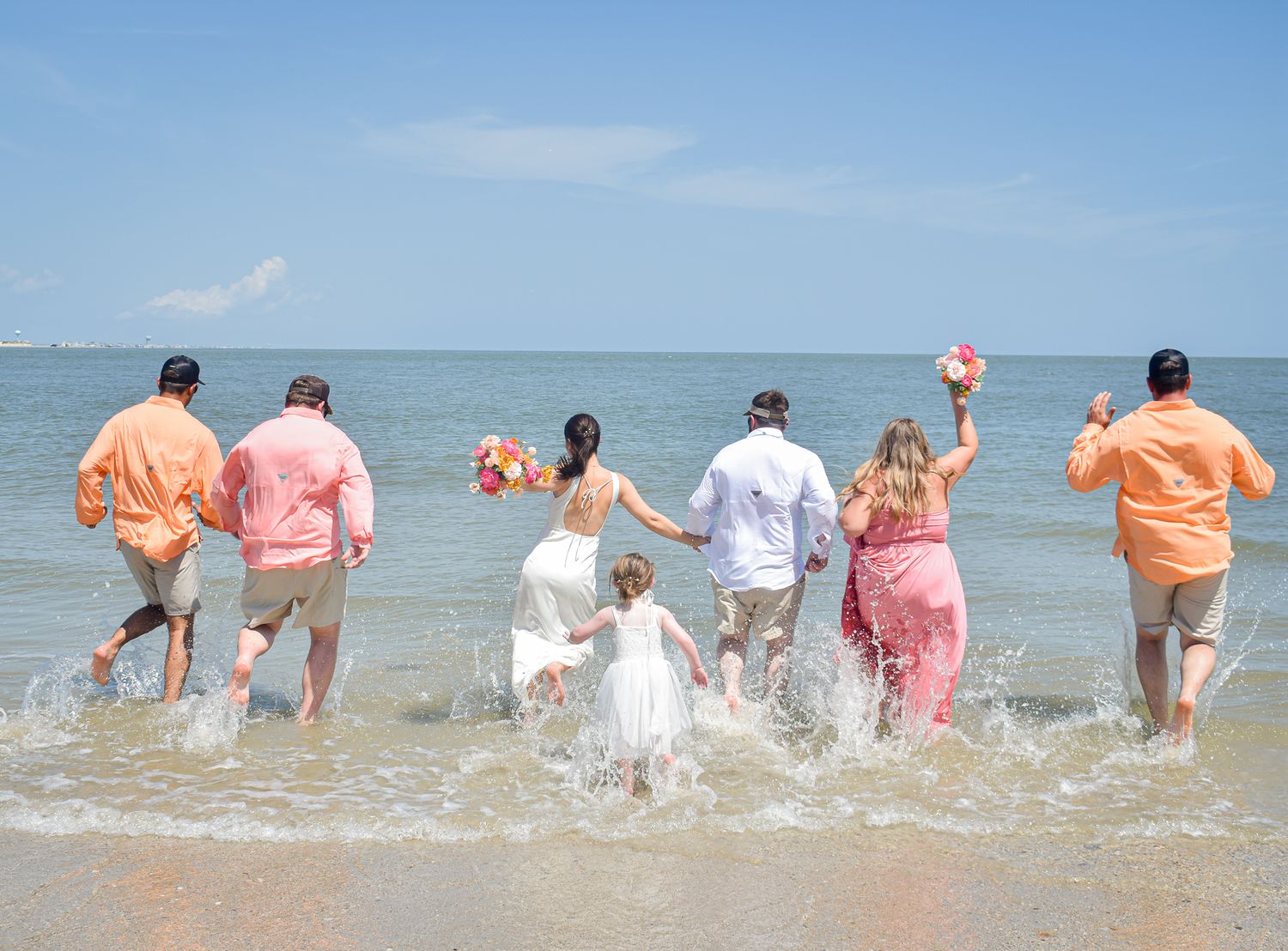Wedding party runs into ocean waves together wearing coordinated beach attire.