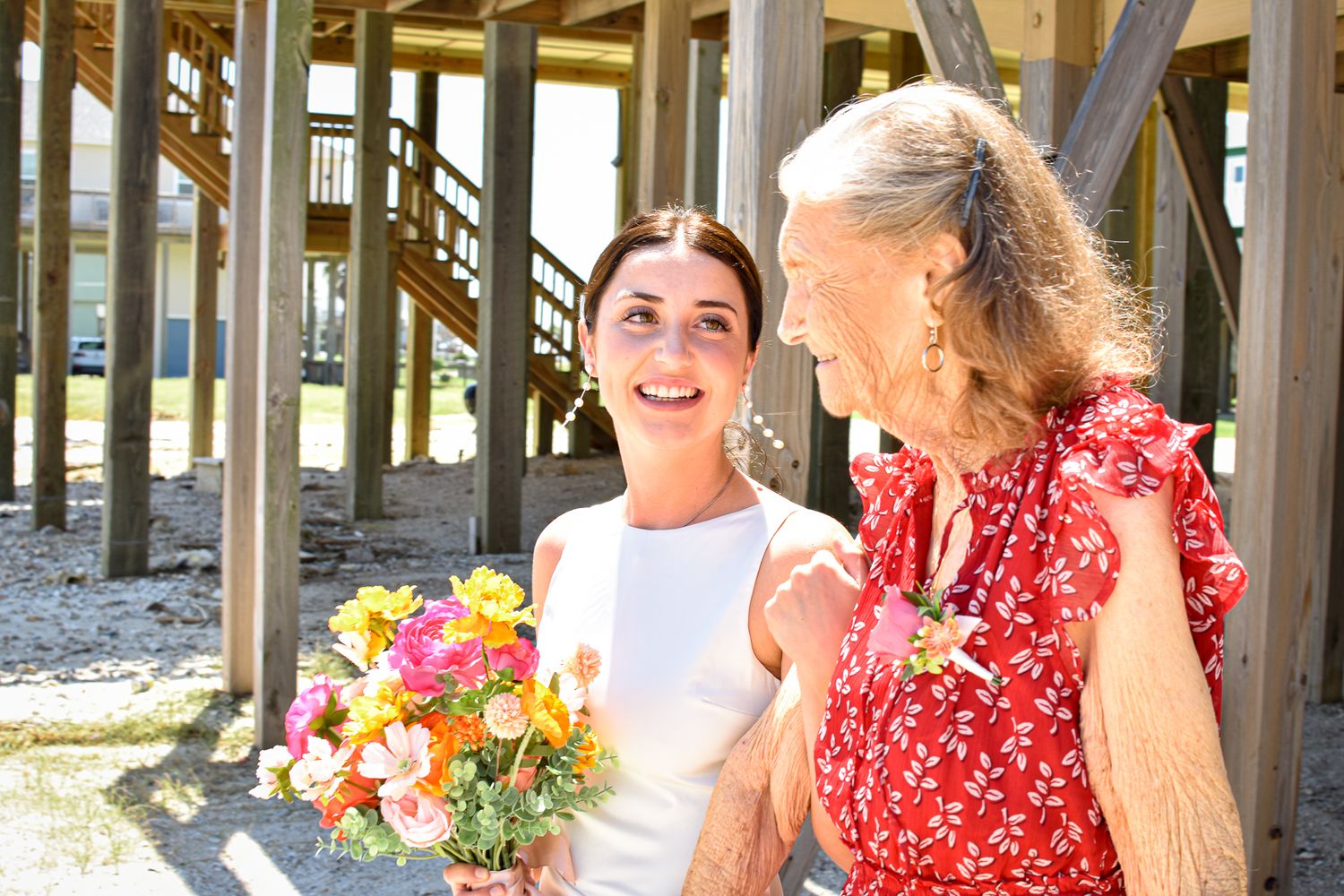 Two people share a laugh while holding colorful bouquets under a wooden pier.