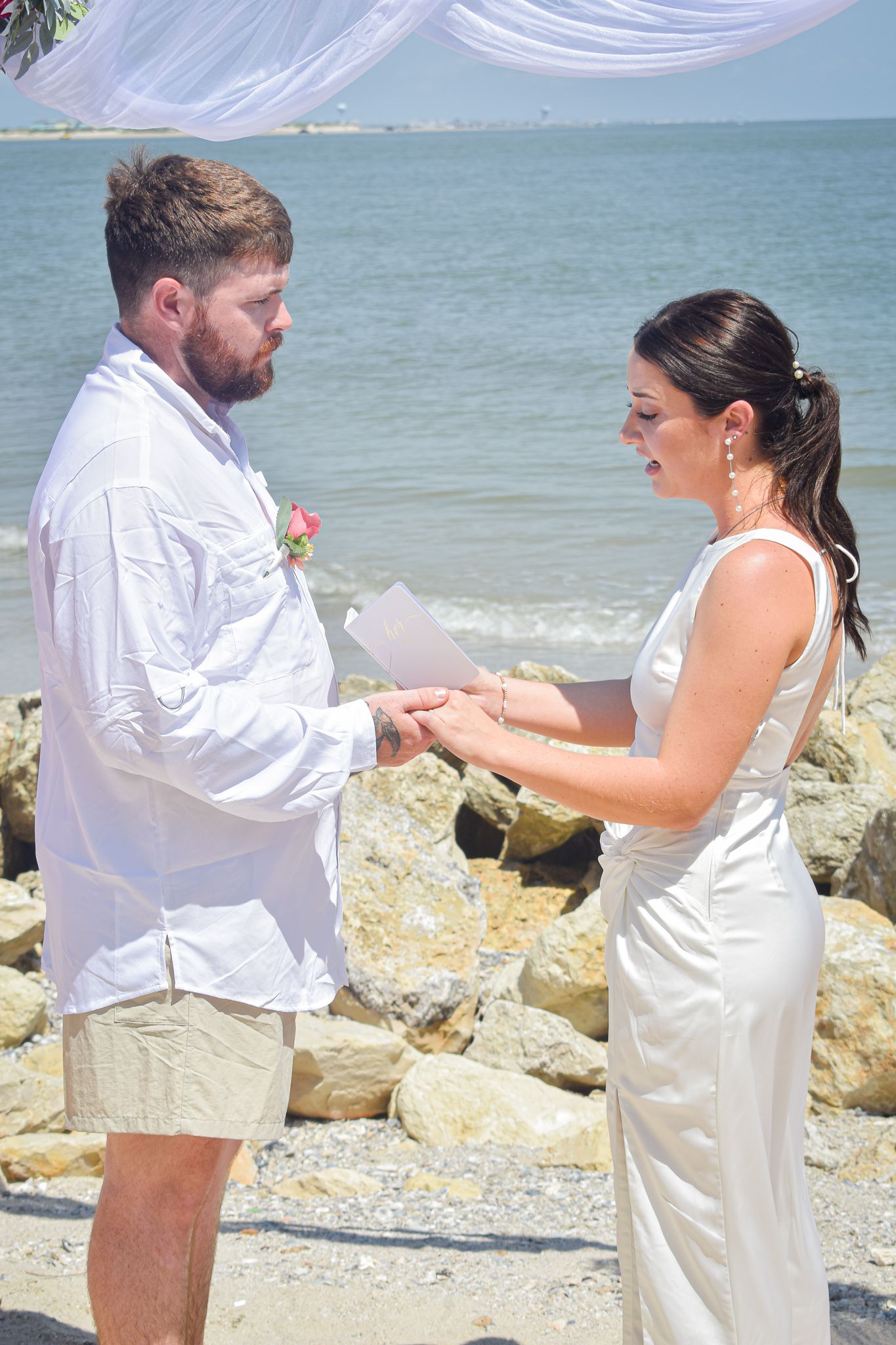 A couple exchanging vows during their beach wedding ceremony with ocean waves in the background.