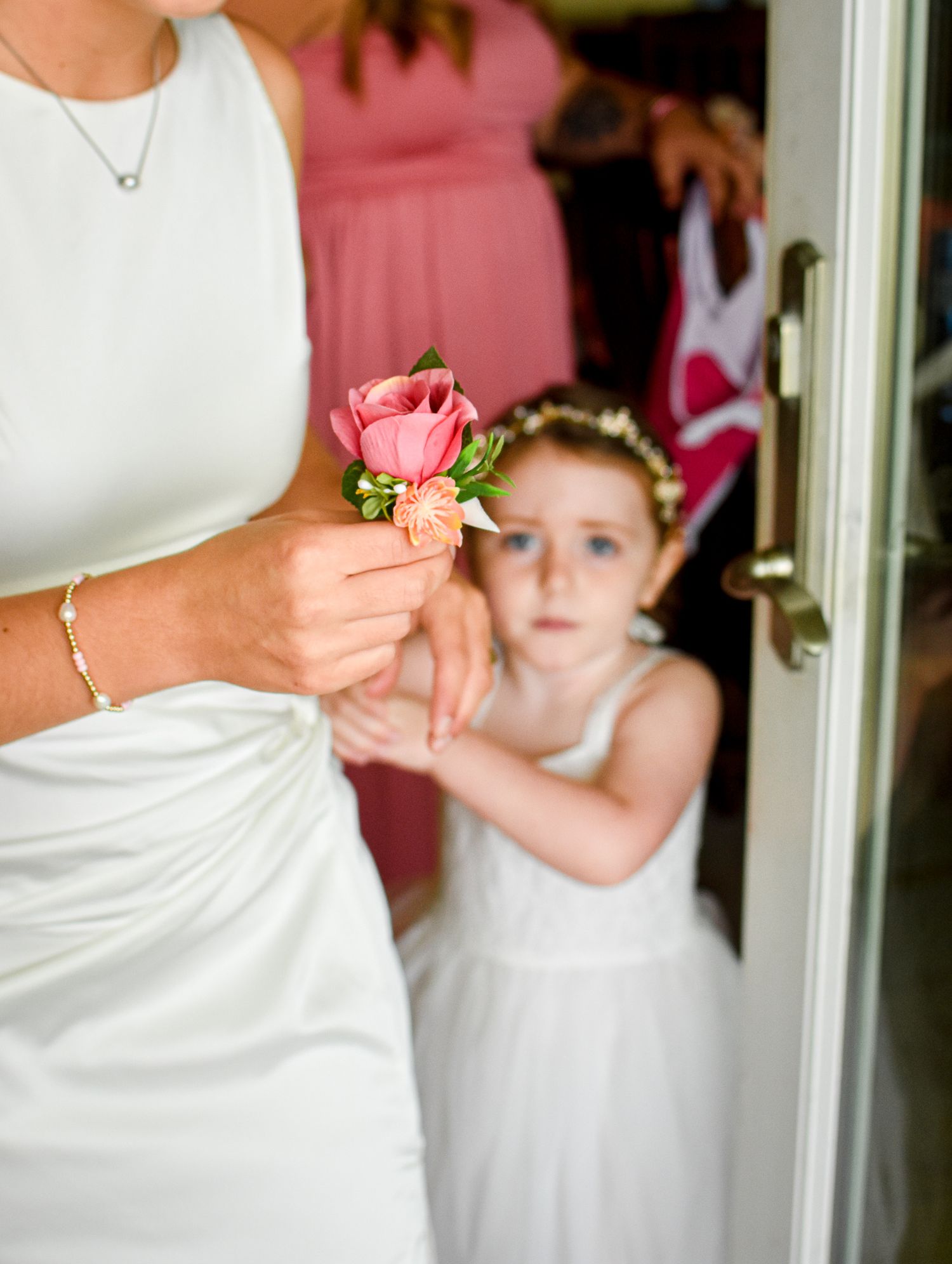 Close-up of a pink rose boutonniere being held against a white wedding dress.