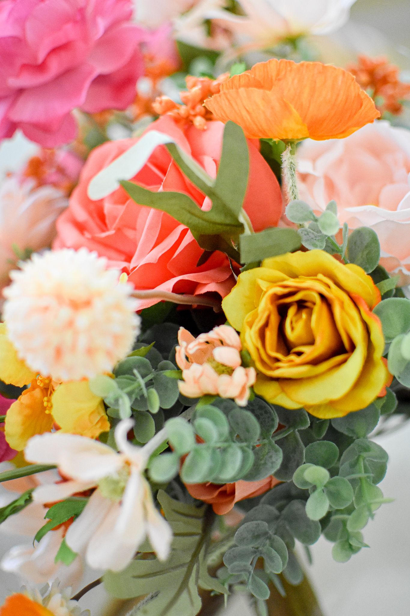 Vibrant floral arrangement with coral, yellow and pink roses mixed with eucalyptus greenery.