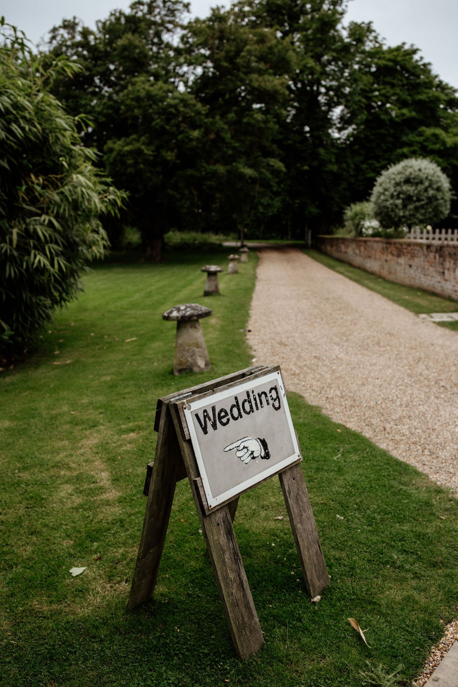 Wooden wedding direction sign on gravel path leading through manicured garden grounds.