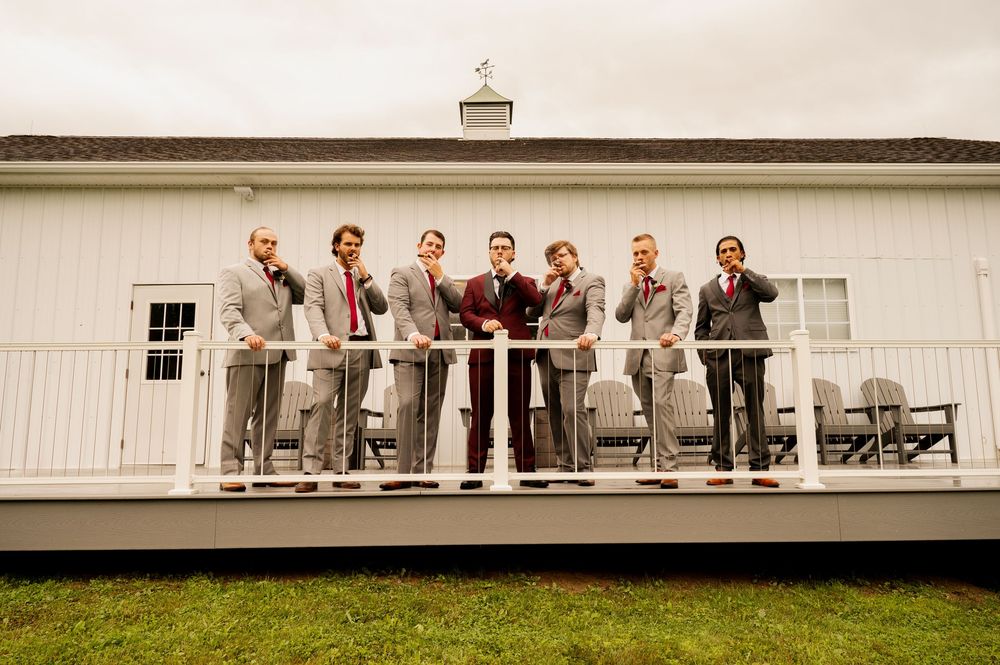 Wedding party members line up across long white building porch on rustic farm property.