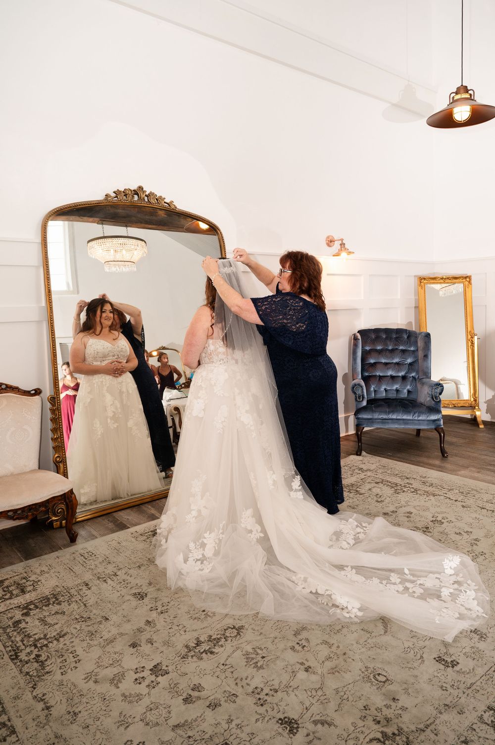 Bride twirls in a white wedding gown with lace details and a flowing train on gray patterned carpet.