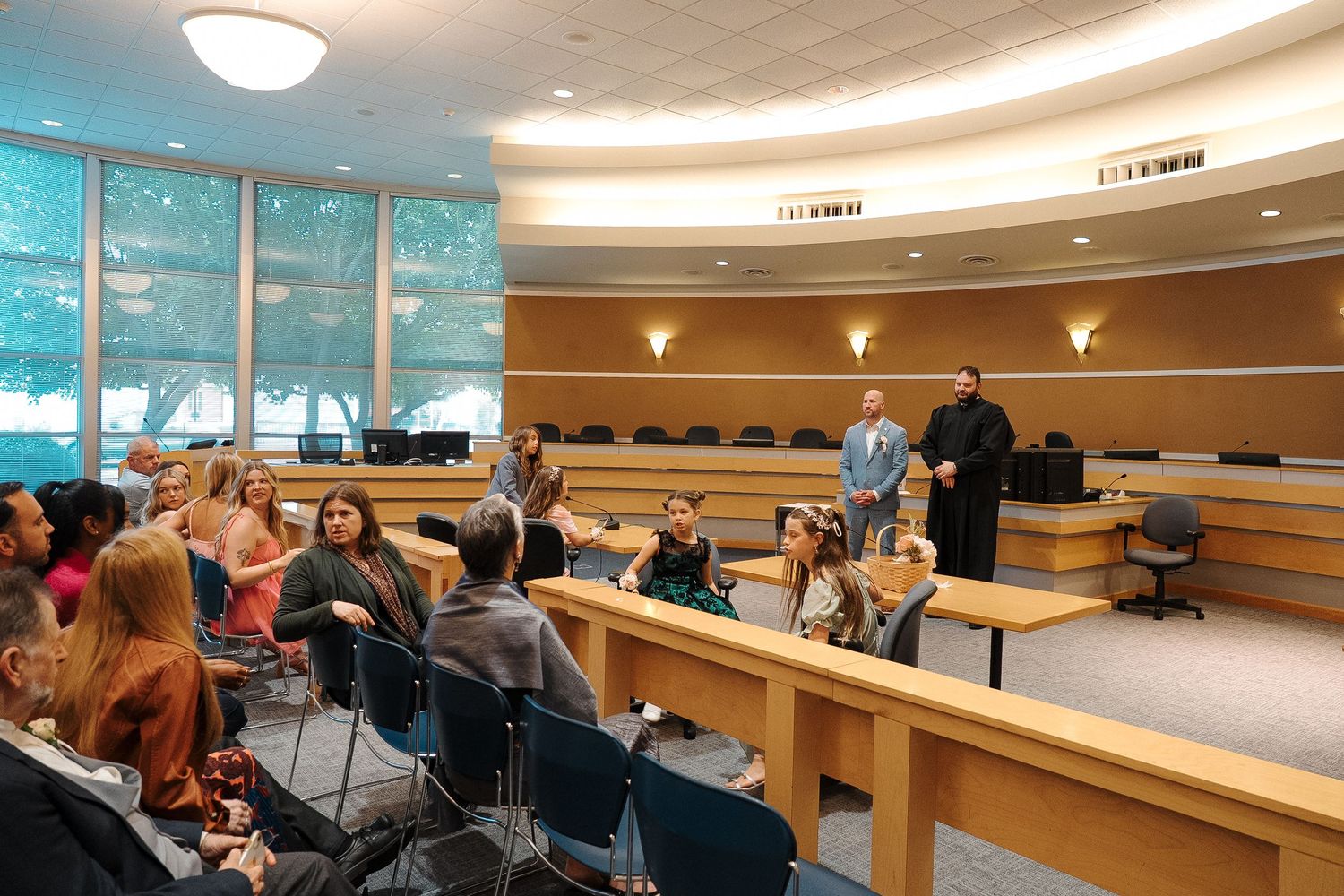 Students sit in a curved lecture hall with tiered seating while attending a presentation in a modern classroom setting.