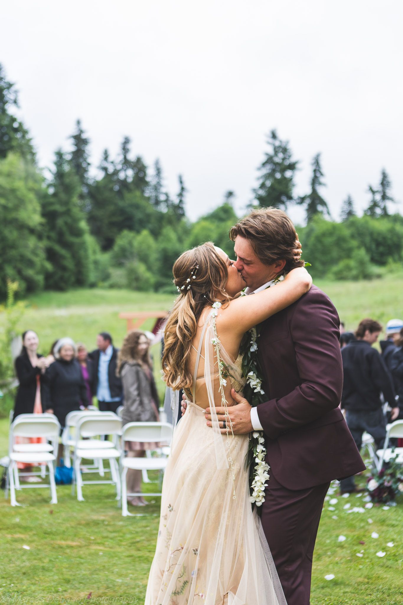 Newlyweds walking hand in hand through a meadow with snow-capped mountains in the background.