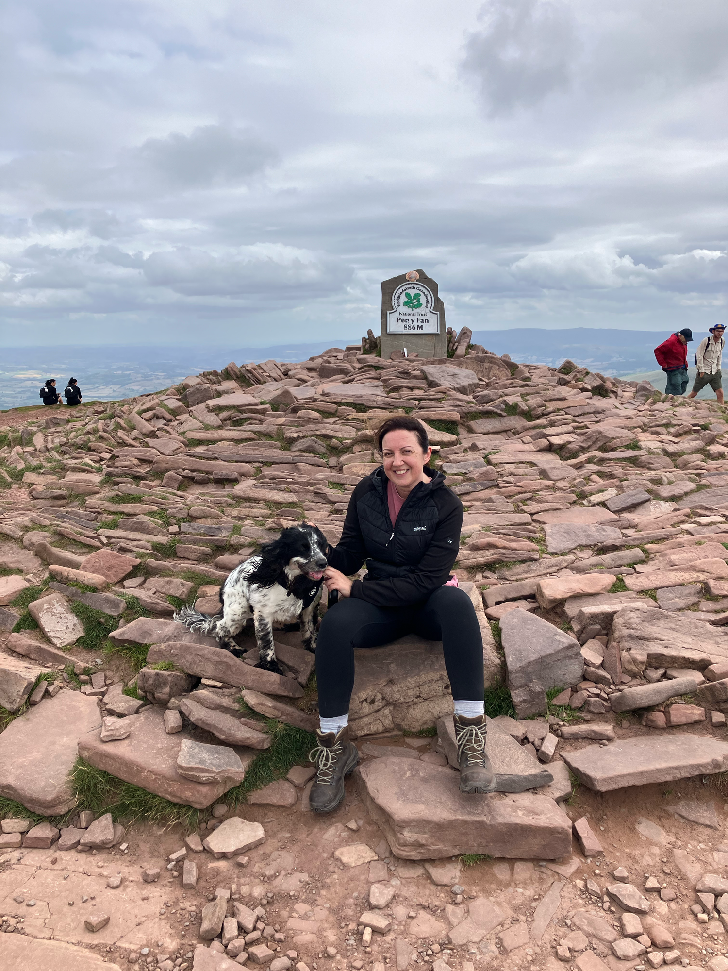a lady and her cocker spaniel at the trig point of pen-y-fan mountain in Wales.