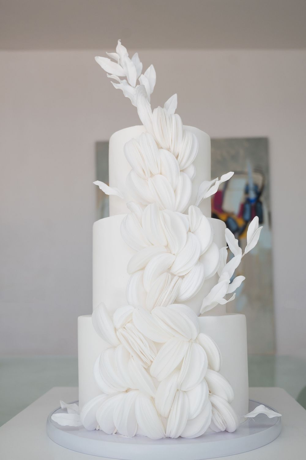 Elegant white wedding cake decorated with dramatic feather-like fondant details cascading down multiple tiers.